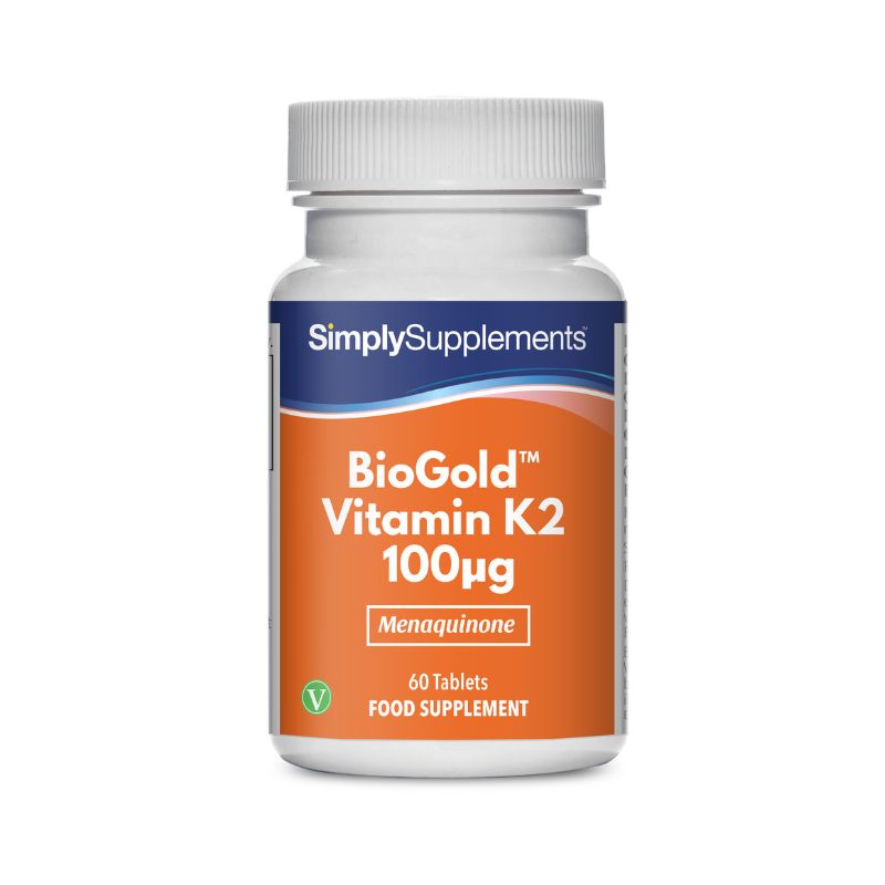 Flacone di integratore etichettato “BioGold Vitamina K2 100mcg Simply Supplements” con etichetta arancione su sfondo bianco.
